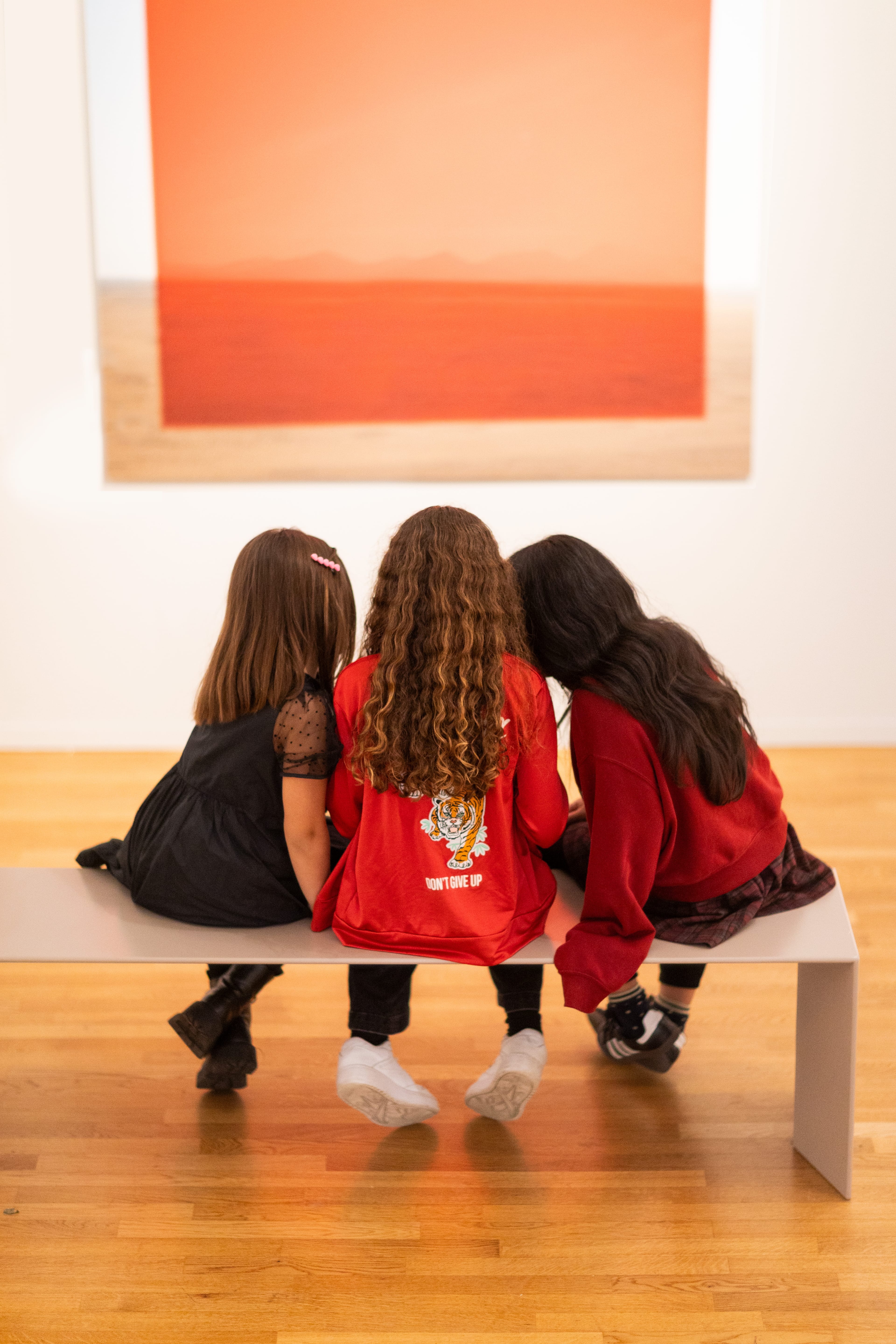 Three girls sitting on a bench looking at a photograph.