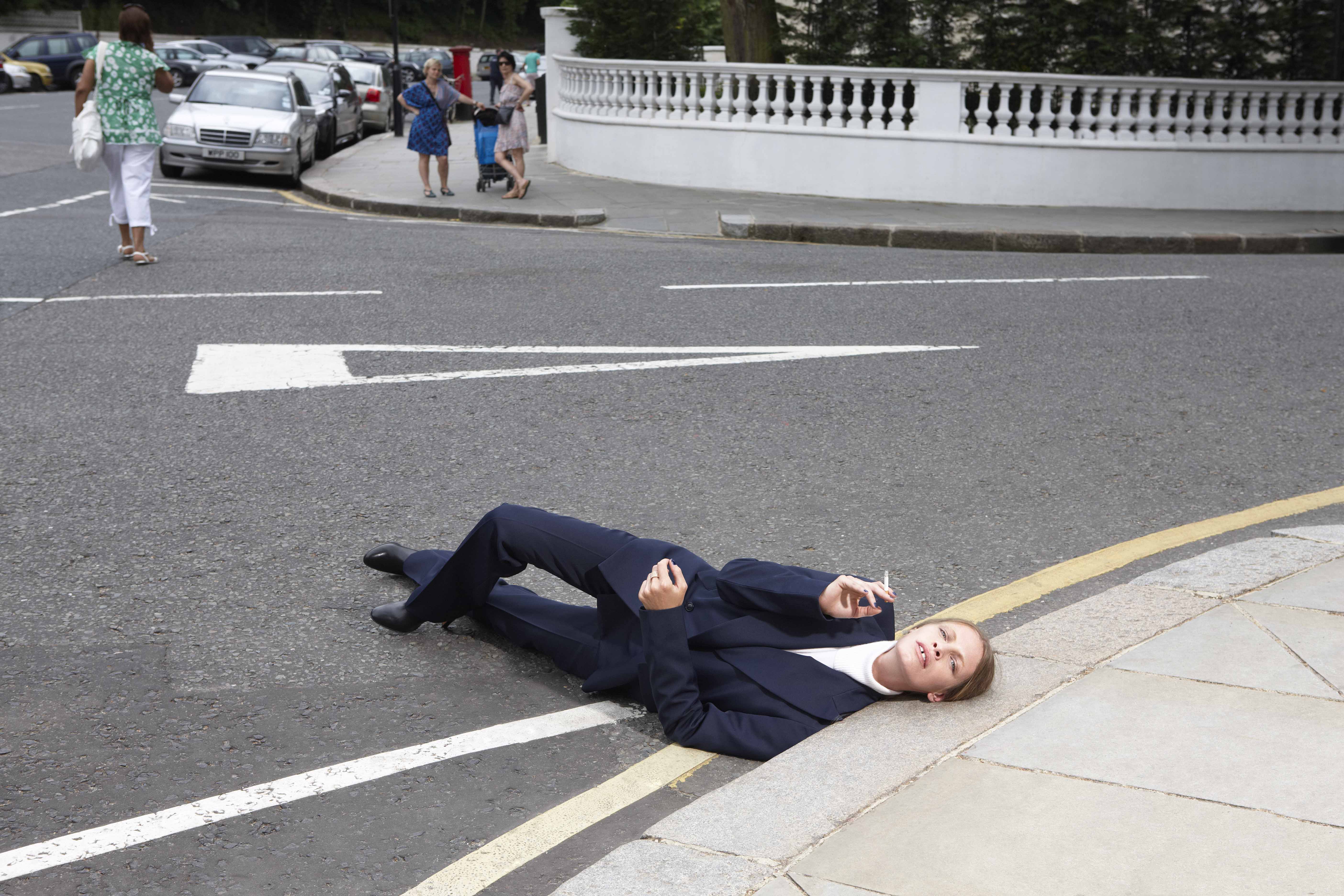 woman smoking on the floor with head on side walk wearing suit